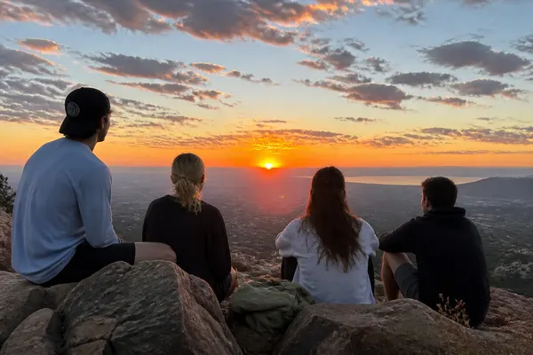 four friends sitting on rocks watching the sun set over a valley