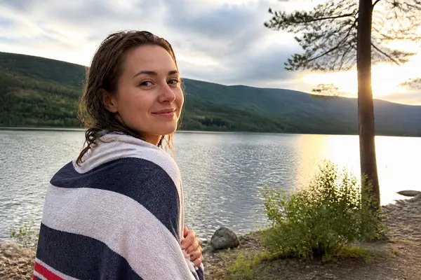 wrapped in a towel by a lake after a swim, hills behind