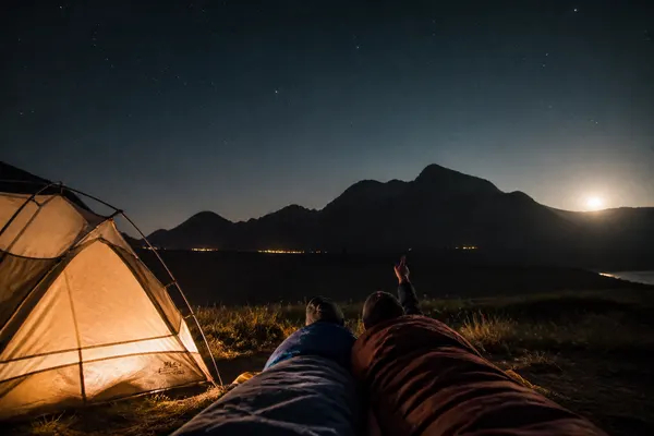 two sleeping bags outside a lit tent under a sky full of stars