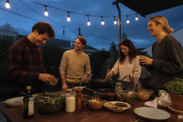 friends cooking round a long garden table under string lights