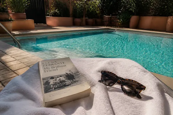 sunglasses and a paperback on a towel beside a pool